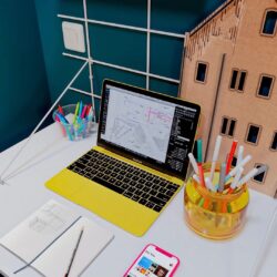Schreibtisch créatif Gassien Paris mit MacBook jaune, maquundte architecturale aus Holz und accessoires colorés.