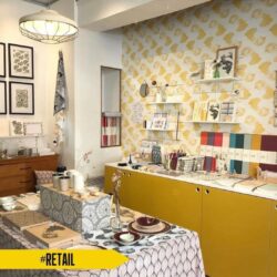 Gassien Paris, mur couleurs en boutique rundail mit Regale weißs, mobilier moutarde und papier peint graphique.
